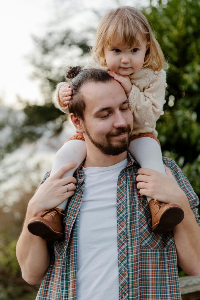 Father carrying daughter on shoulders outdoors in a park. Happy and bonding moment.