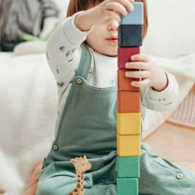 Child in White Long-sleeve Top and Dungaree Trousers Playing With Lego Blocks