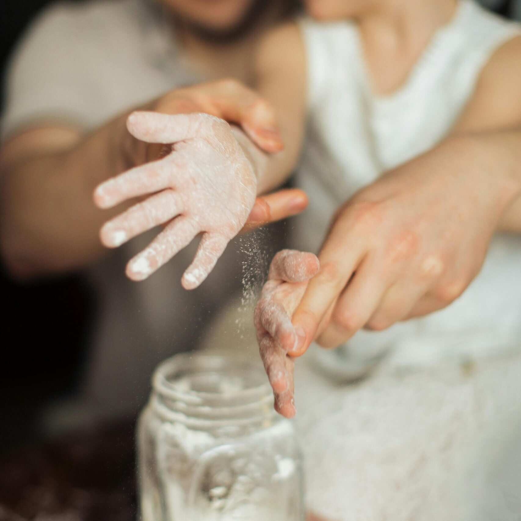 Happy crop cute girl with pigtail and blurred father shaking off flour from hands while making dough