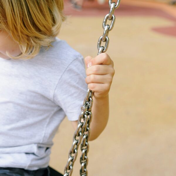 A Kid Sitting on a Swing while Holding on a Metal Chain